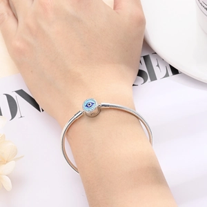 Silver beaded snake chain bracelet with blue evil eye charm worn on a female wrist