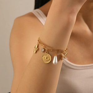 Détail d'un bracelet doré multicouche avec breloques papillon, perle et fleur sur deux chaînes