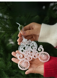 Close-up of a pink hollow carriage ornament held in front of a Christmas tree