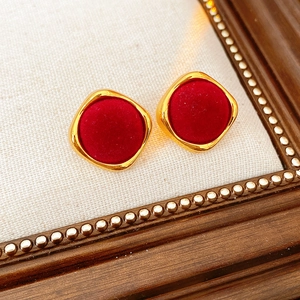 Détail de boucles d'oreilles losanges floquées dorées sur fond de tissu texturé