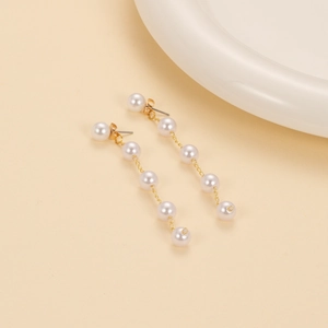 Detailed close-up of long gold chain tassel earrings with gradient white pearls