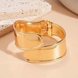 Dettaglio di un ampio bracciale rigido geometrico dorato con chiusura a cerniera