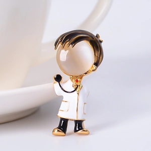 Close-up of a cartoon doctor brooch with white enamel finish and gold metal accents