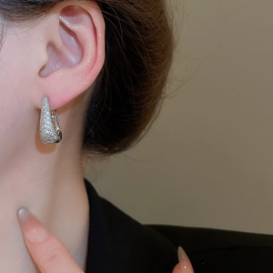Gros plan de boucles d'oreilles en U argentées avec zircons portées par un mannequin chic