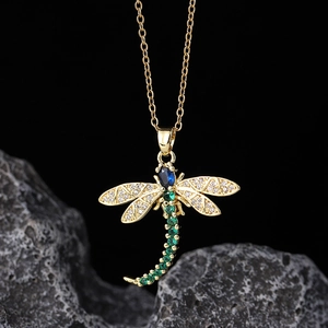 Detailed close-up of a gold dragonfly pendant with vibrant green and blue gemstones