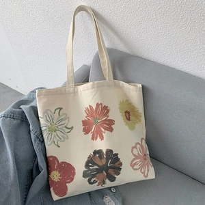 Detailed shot of beige floral canvas tote bag resting on a sofa with hand-painted flowers