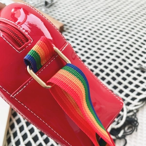 Close-up of vibrant red patent leather bag with rainbow canvas strap and gold hardware