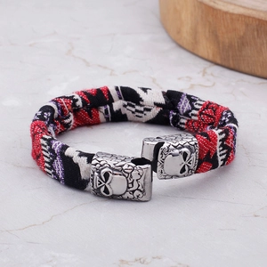 Detail of woven textile bracelet featuring silver metal skull clasps on marble surface