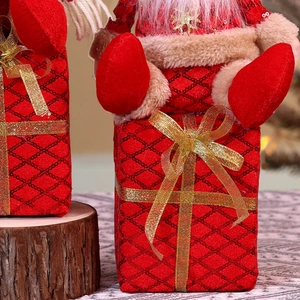 Detail of red quilted Christmas gift box with golden bow and plush Santa topper