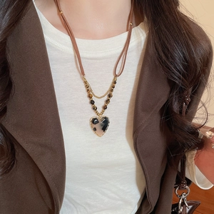 Detail of leopard print heart pendant on double-layer brown leather and gold beaded chain