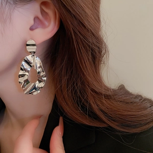 Detail of silver irregular wavy textured earrings worn by a model in a close-up profile