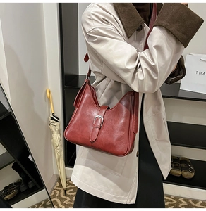 Vue latérale d'un sac hobo en cuir bordeaux avec boucle argentée porté par un modèle