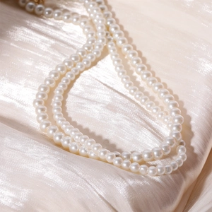 Elegant multi-strand white glass pearl necklace displayed on luxurious champagne silk fabric