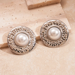 Close-up of silver textured flower studs with white pearl center on stone background