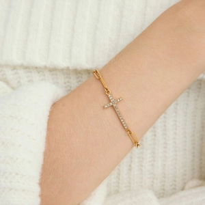 Elegante gouden paperclip armband met witte zirkoon kruis gedragen om de pols