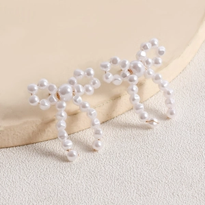 Detail of handmade woven pearl bow earrings with elegant golden wire accents and tassels