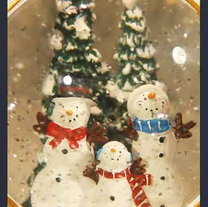 Close-up of a festive Christmas snow globe featuring snowman family and snowy pine trees