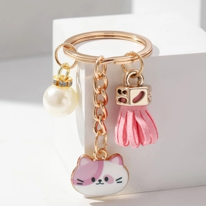 Close-up of golden keychain with pink cat pendant, white pearl, and soft silk tassel