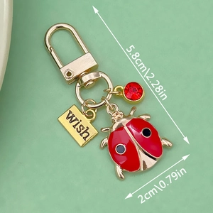 Golden ladybug keychain with red gemstone and engraved Wish charm on green surface