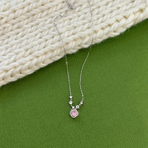 Detail of pink square zircon pendant on silver necklace over green textured backdrop