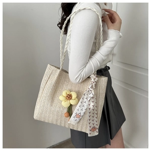 Detail of woven bucket bag featuring decorative floral charm and silk scarf on a model
