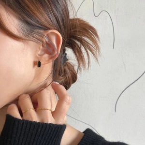 Detail of black rectangular zircon earrings and thin gold rings on a female model