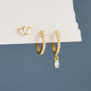 Close-up of golden crown stud and zircon hoop earrings set on textured white paper