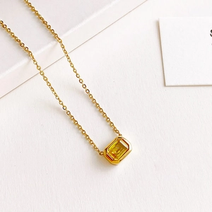 Elegante collar de oro con un colgante rectangular de gema amarilla sobre fondo blanco