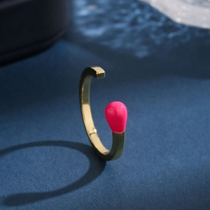 Elegant gold open bangle with pink enamel match-head detail on a dark blue textured surface
