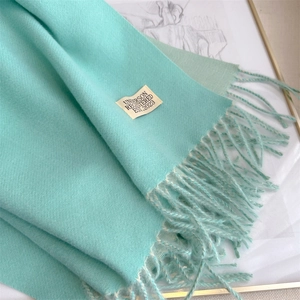 Detail showing the soft texture and fringe of a light blue cashmere scarf with a label