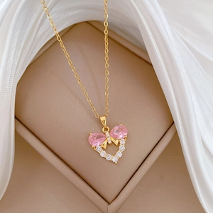 Gold titanium necklace with pink bow and white zircon heart pendant on silk cloth