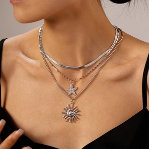 Detail of layered silver necklace featuring starfish charm and sun face pendant on model