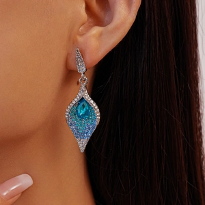 Close-up of teardrop earrings with blue crystals and silver metal on a model ear