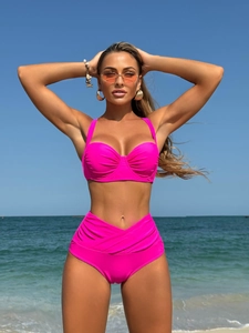 Detail of hot pink bikini featuring ruched high-waist bottoms and textured cups on a beach