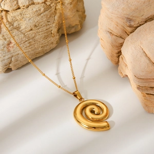 Close-up of golden spiral shell pendant on a thin chain over textured stones