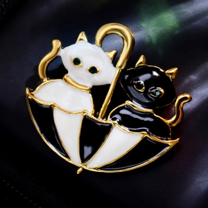 Close-up of a black and white cat pair under an umbrella brooch with gold metal details