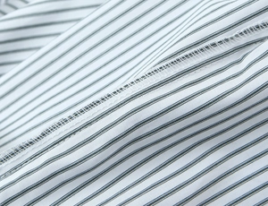 Detailed close-up of blue and white striped poplin fabric with professional overlock stitching