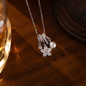Macro shot of a silver titanium necklace with zircon flower and pearl on wood