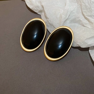 Détail de boucles d'oreilles ovales vintage avec résine noire et cadres dorés mats
