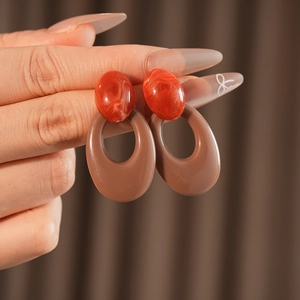 Detail shot of vintage oval earrings in orange and brown resin held by a hand