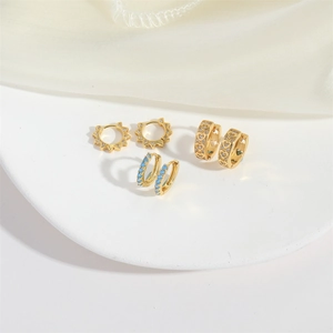 Three pairs of elegant gold earrings with heart and sunflower designs on a white silk base