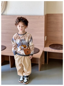 Full body shot of child in tie-dye NASA hoodie and beige pants with a bear crossbody bag