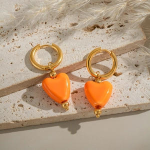 Boucles d'oreilles créoles dorées avec cœurs oranges sur une plaque de pierre texturée