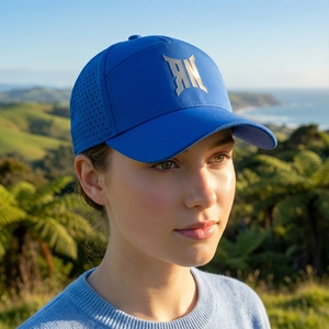 Navy blue breathable baseball cap with metal logo against scenic coastal background