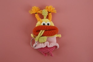 Close-up of yellow handmade crochet monster key cover with orange lips and pink skirt