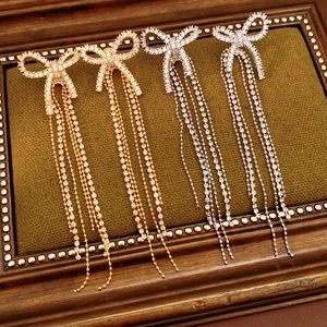 Detailed view of 18k gold plated bow tassel earrings with sparkling cubic zirconia on wood