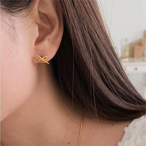 Macro detail of gold bow stud earrings with twisted rope texture worn by a model