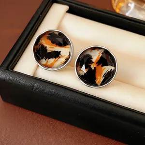 Faceted round leopard print earrings with silver pins on a black jewelry display