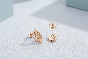 Close-up of rose gold leaf earrings set against a clean white and green background