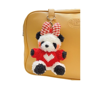 Porte-clés panda en peluche avec pull rouge tricoté et nœud sur un sac en cuir